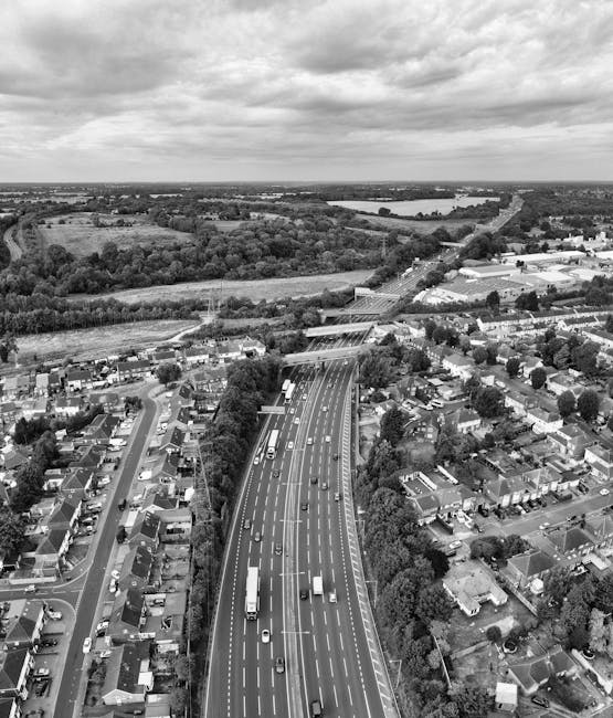 A black-and-white aerial view of a residential area showing closely packed houses with pitched roofs, some brick-built, along with commercial or industrial buildings situated on the outskirts. Streets