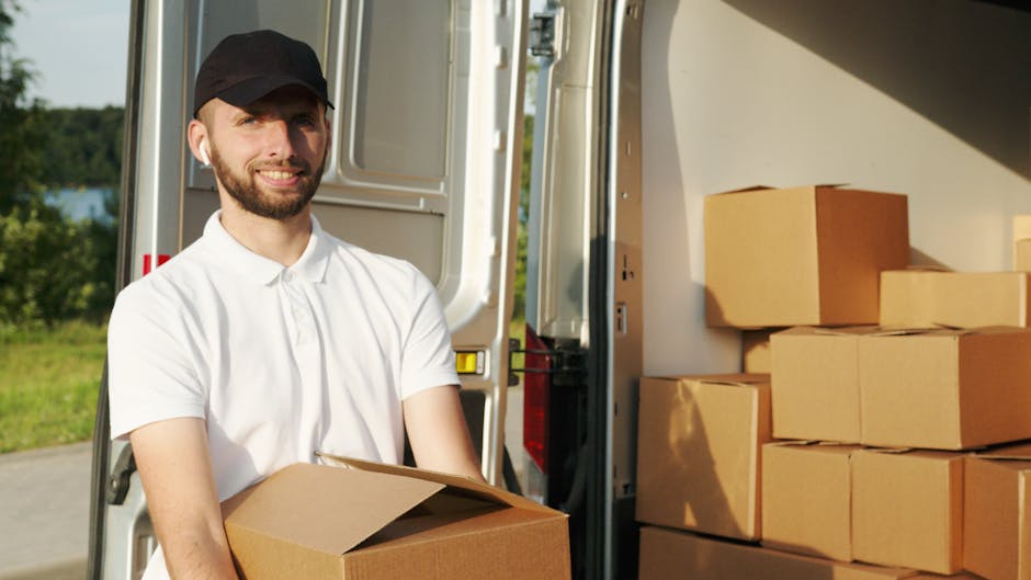A woman wearing a white cap and a black sleeveless top is depicted outdoors, holding a clipboard and appearing to take notes or record details. She is standing near several cardboard boxes, some closed and others open, which are stacked or positioned on the pavement near her. A man, seen partially, is holding a medium-sized cardboard box, preparing for or engaged in the home relocation process. The scene takes place on a paved area with a blurred background, possibly within a residential environment, during daylight hours with natural lighting. This image illustrates the packing and moving coordination involved in house removals, with the presence of packaging materials, boxes, and the involvement of personnel from Man with Van Aldborough Hatch, a company specialising in efficient furniture transport and removal services geared towards urgent same-day relocations.